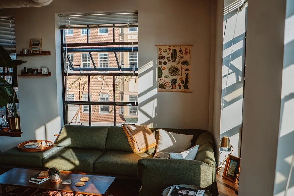 A sunlit sitting room with a low table, patterned rug and a deep sofa under tall windows.