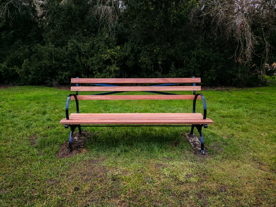 A slatted hardwood bench with cast-iron ends standing on grass in front of a dark hedge.