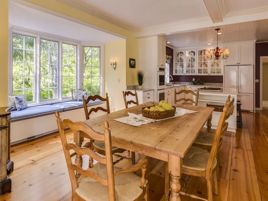 A long pine dining table with six ladder-back chairs, set in a bay window overlooking a garden.