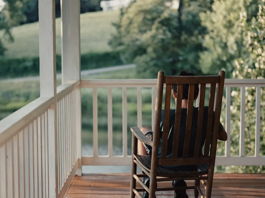 Someone resting in a tall oak rocking chair on a shaded porch, looking out over a green lawn.